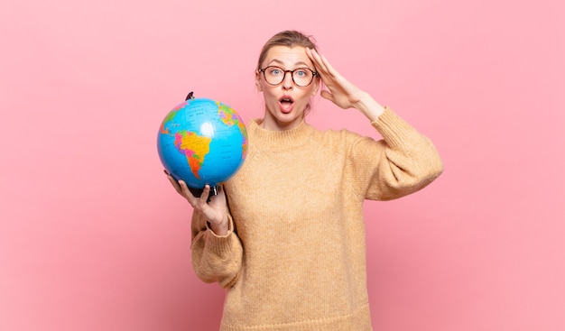 Young blond woman looking happy, astonished and surprised, smiling and realizing amazing and incredible good news. world concept