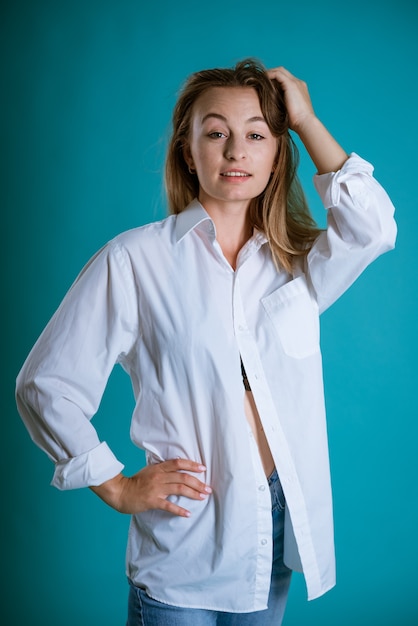 Young blond woman posing in a white shirt and jeans on a blue wall