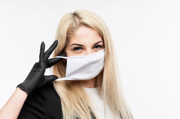 Young blond woman puts on a medical mask. Close-up. Isolated on white wall.