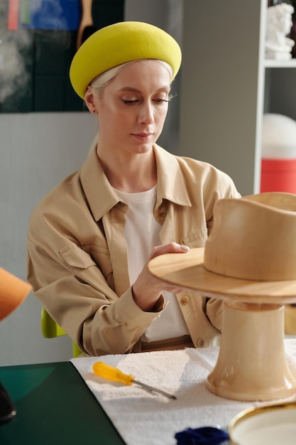 Young blond woman putting wooden workpiece of hat on thick stem