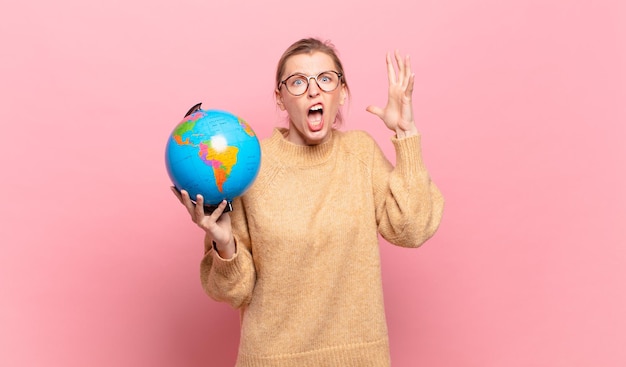 Young blond woman screaming with hands up in the air feeling furious frustrated stressed and upset world concept