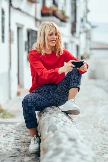 Young blond woman sitting using smart phone.