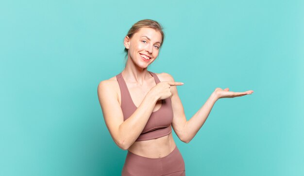 Young blond woman smiling cheerfully and pointing to copy space on palm on the side, showing or advertising an object. sport concept