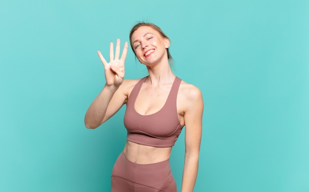 Young blond woman smiling and looking friendly, showing number four or fourth with hand forward, counting down. sport concept