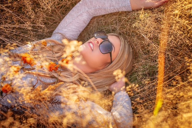 Young blond woman in sunglasses lying in golden grass.