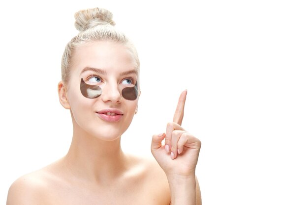 young blond woman with black eye patches points finger at copy space isolated on white background