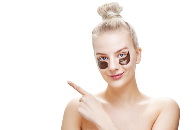 young blond woman with black eye patches points finger at copy space isolated on white background