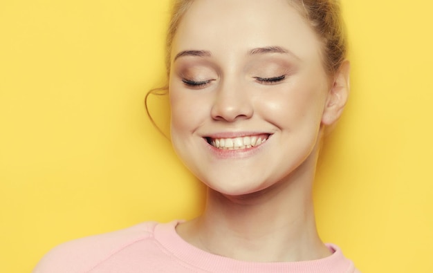 Young blond woman with closed eyes over yellow background