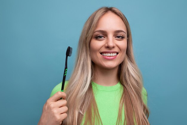 Young blond woman with healthy teeth holding a toothbrush on a blue background