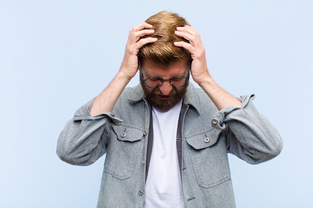 Giovane uomo adulto biondo sentirsi stressato e frustrato, alzando le mani alla testa, sentendosi stanco, infelice e con emicrania