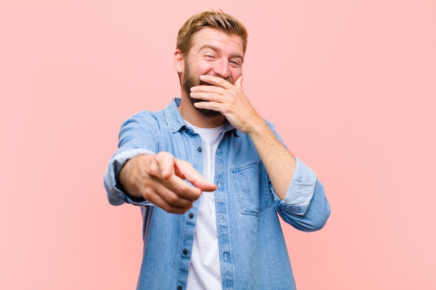 Young blonde adult man laughing at you, pointing to camera and making fun of or mocking you