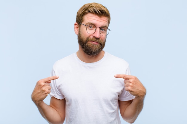 Young blonde adult man looking proud, positive and casual pointing to chest with both hands