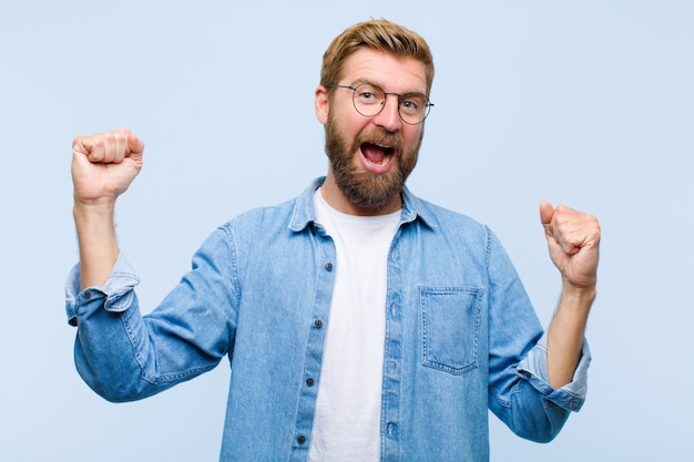 Giovane uomo adulto biondo che grida trionfalmente, sembrando vincitore eccitato, felice e sorpreso, celebrante