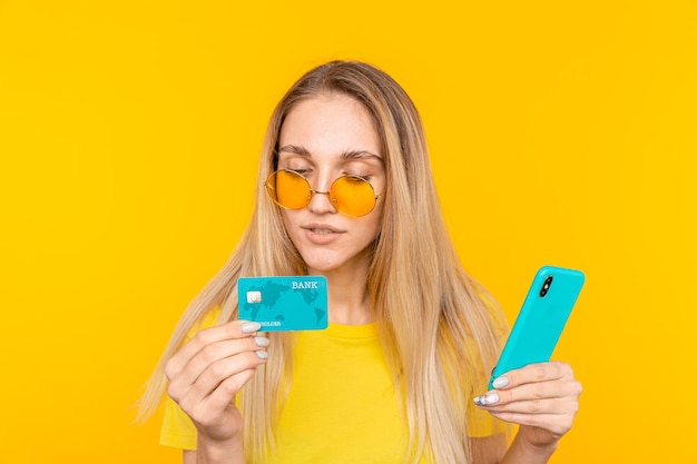 Фото Молодая блондинка aoman держит кредитную карту и использует смартфон на желтом