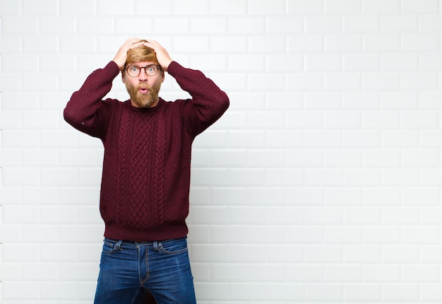 Photo young blonde bearded man raising hands to head and panicking at a mistake