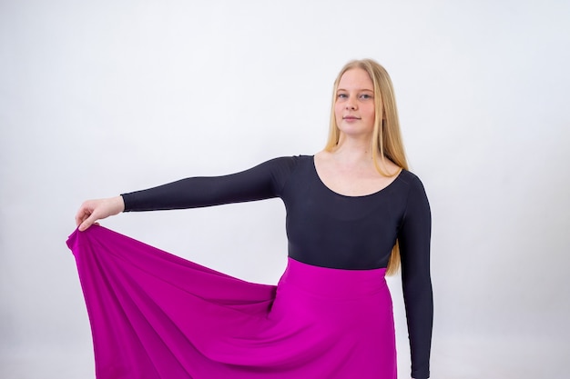 Young blonde blue-eyed dancer woman in long purple skirt on white background