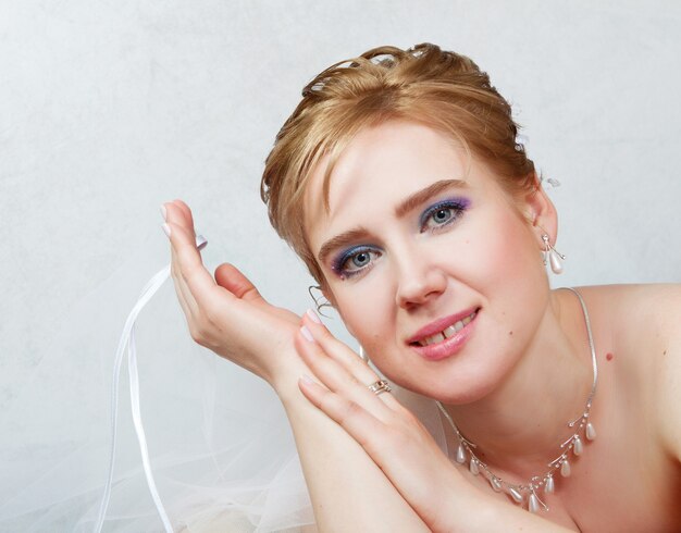 Young blonde bride smiling holding a veil in her hand. Close-up portrait.