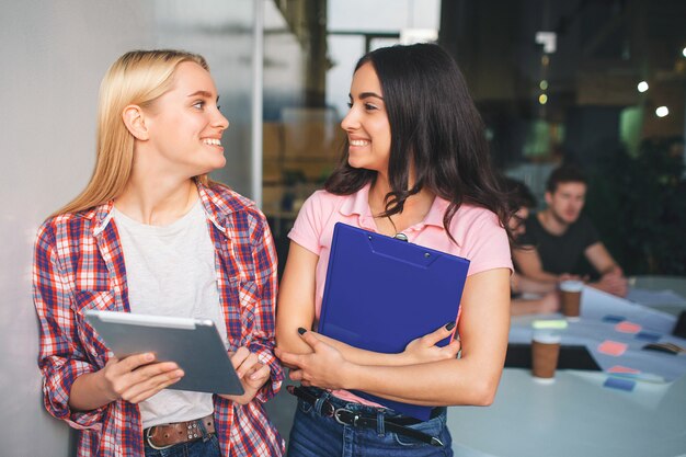 Young blonde and brunette women stand together and smile