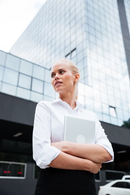 Young blonde business woman with tablet standing near her office outdoors