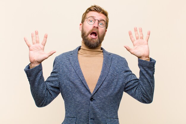 Young blonde businessman feeling stupefied and scared, fearing something frightening, with hands open up front saying stay away