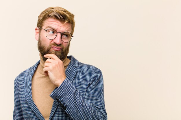 Young blonde businessman thinking, feeling doubtful and confused, with different options, wondering which decision to make