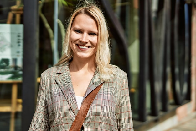 Young blonde businesswoman smiling happy standing at the city.