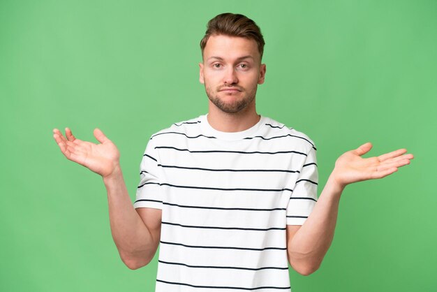 Young blonde caucasian man over isolated background having doubts while raising hands