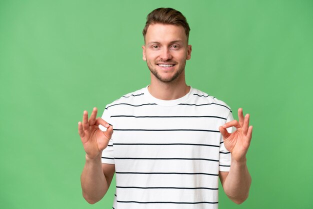 Young blonde caucasian man over isolated background showing ok sign with two hands