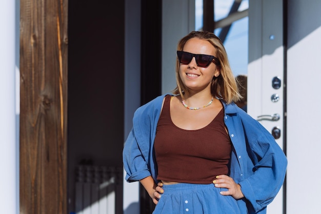 Photo young blonde caucasian woman in casual dress standing outdoors at opened door waiting for husband to