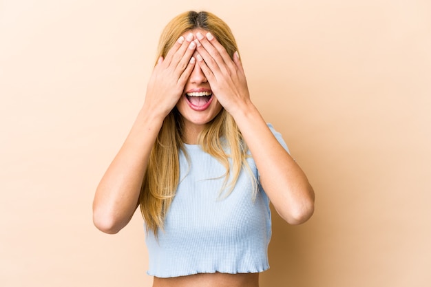 Young blonde caucasian woman covers eyes with hands, smiles broadly waiting for a surprise.