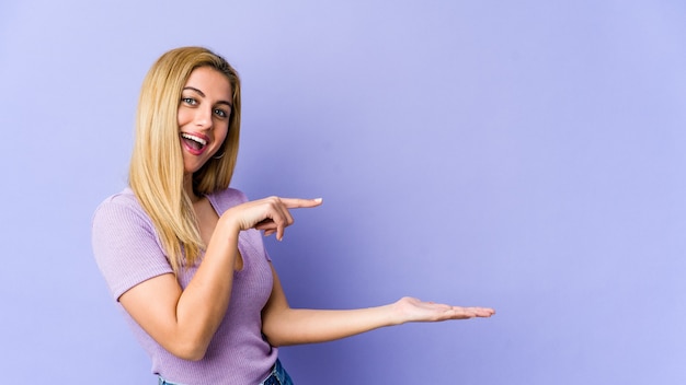 young blonde caucasian woman excited holding a copy space on palm.