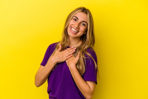 Young blonde caucasian woman   has friendly expression, pressing palm to chest. Love concept.