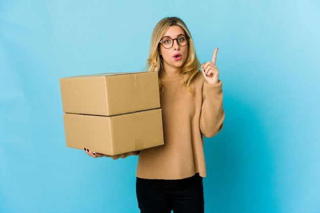 Young blonde caucasian woman holding boxes to move having some great idea, concept of creativity.