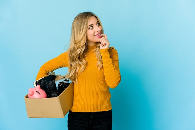Young blonde caucasian woman holding boxes to move relaxed thinking about something looking at a copy space.