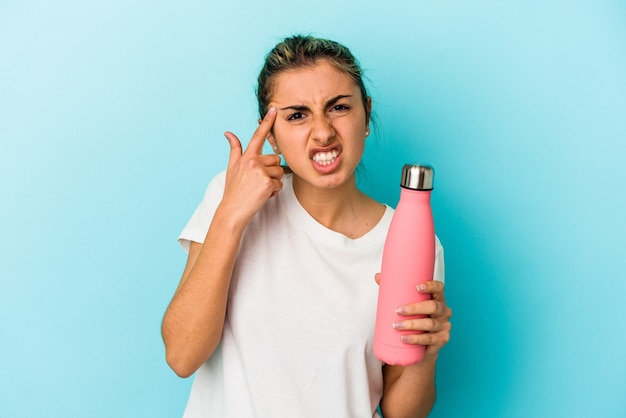 Young blonde caucasian woman holding a thermo isolated on blue wall showing a disappointment gesture with forefinger