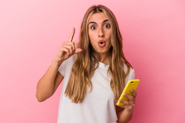 Young blonde caucasian woman holding a yellow mobile phone isolated having an idea, inspiration concept.