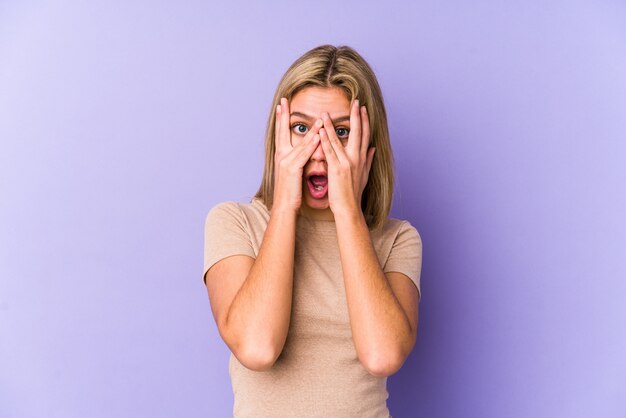 Young blonde caucasian woman isolated blink through fingers frightened and nervous.