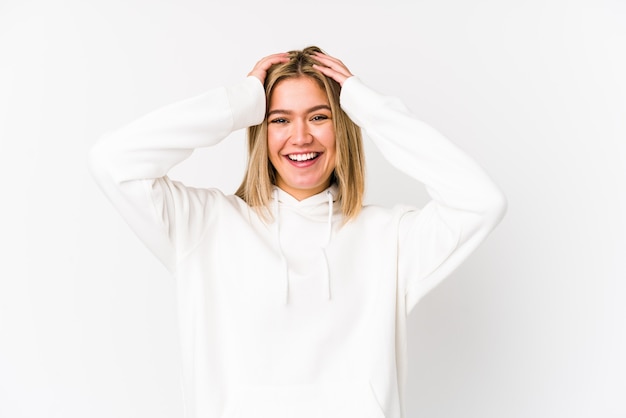 Young blonde caucasian woman isolated laughs joyfully keeping hands on head. Happiness concept.