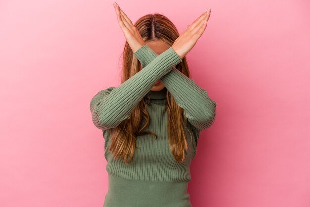 Young blonde caucasian woman isolated on pink background keeping two arms crossed, denial concept.