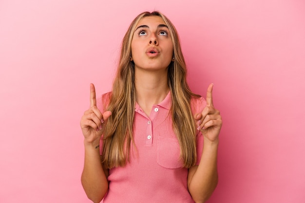 Young blonde caucasian woman isolated on pink background pointing upside with opened mouth