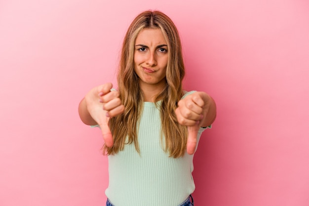 Young blonde caucasian woman isolated on pink background showing thumb down and expressing dislike.