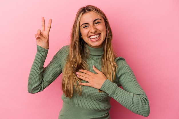 Young blonde caucasian woman isolated on pink wall taking an oath, putting hand on chest