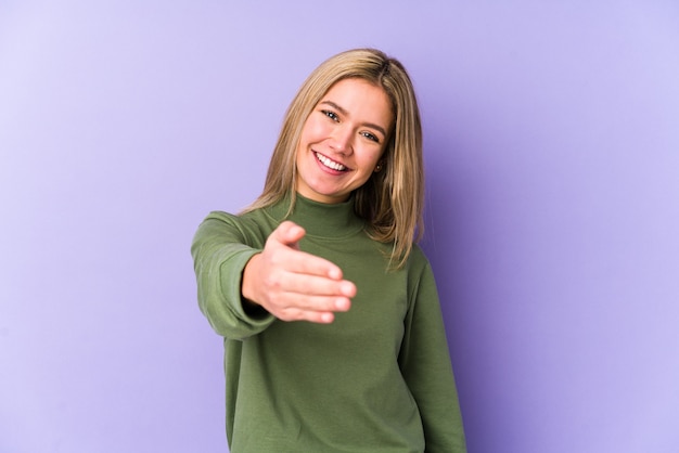 Young blonde caucasian woman isolated stretching hand in greeting gesture.