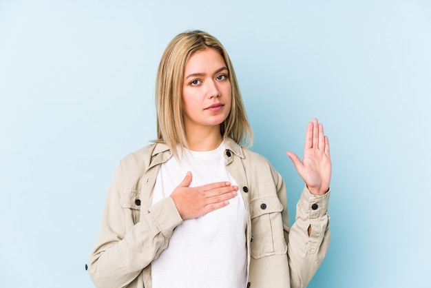 Giovane donna bionda caucasica isolata prestando giuramento, mettendo la mano sul petto.