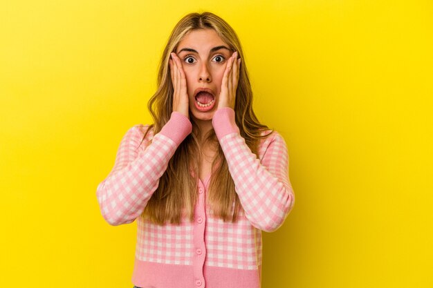 Young blonde caucasian woman isolated on yellow background surprised and shocked.