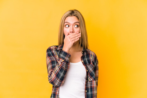 Young blonde caucasian woman isolated on yellow shocked covering mouth with hands.