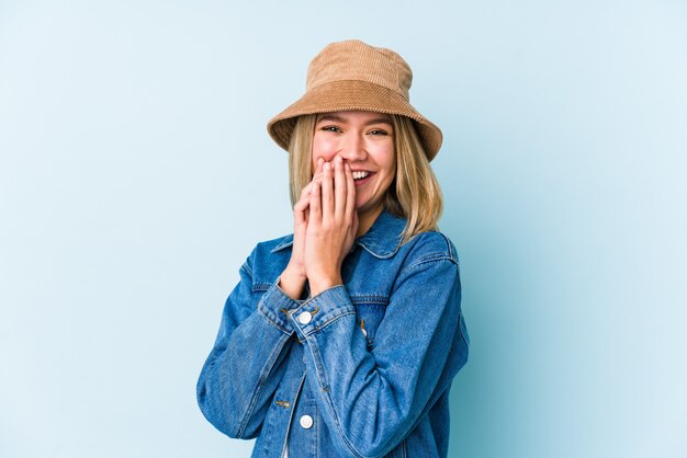 Young blonde caucasian woman laughing about something, covering mouth with hands.