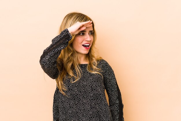 Young blonde caucasian woman looking far away keeping hand on forehead.