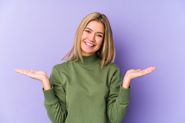 Young blonde caucasian woman makes scale with arms, feels happy and confident.