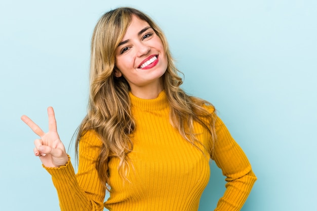 Young blonde caucasian woman showing victory sign and smiling broadly.